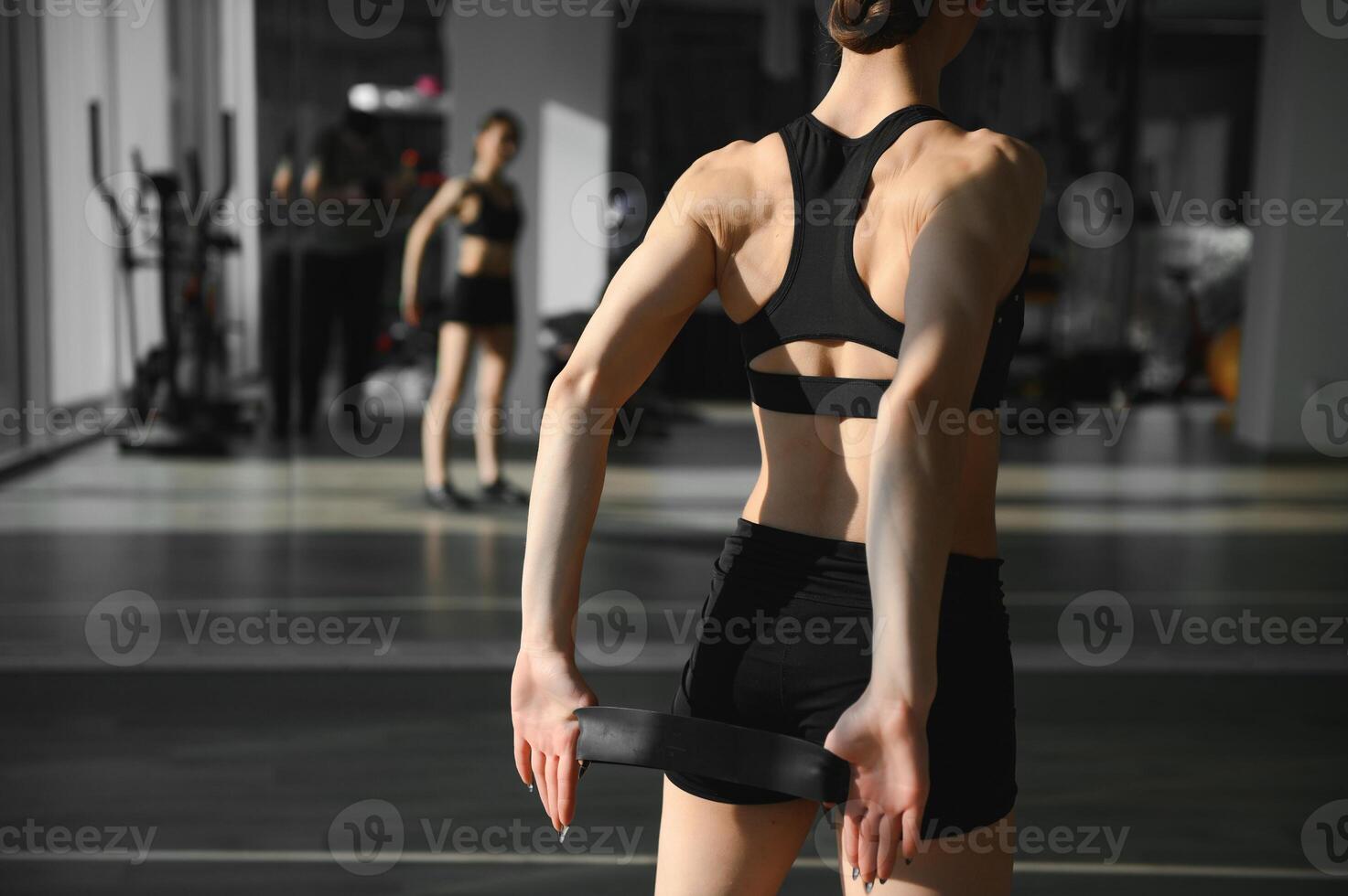 Motivation for girls. Modern young woman in sport clothing crouching using resistance band while exercising in the gym. photo