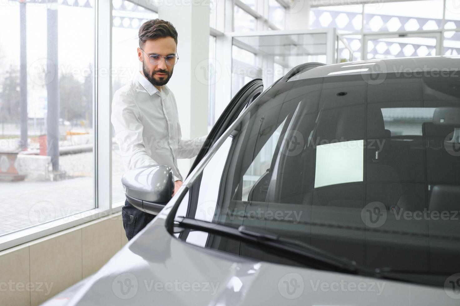 Happy young guy checking new luxury car, buying automobile at dealership centre. Portrait of cheerful millennial Caucasian man examining auto at showroom store photo