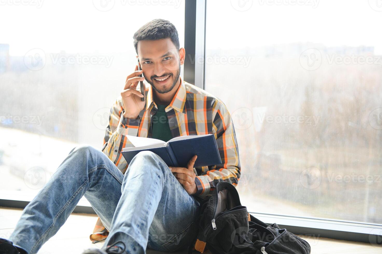 Young indian student boy reading book studying in college library with bookshelf behind. working on assignment or project photo