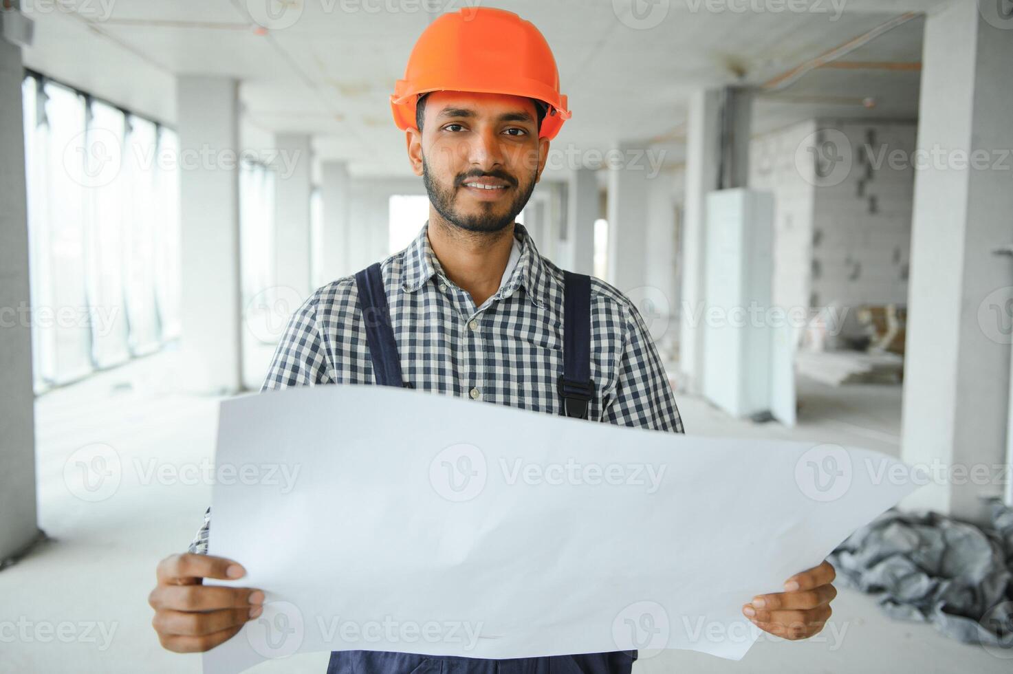 Indian construction site manager standing wearing helmet, thinking at construction site. Portrait of mixed race manual worker or architect. photo