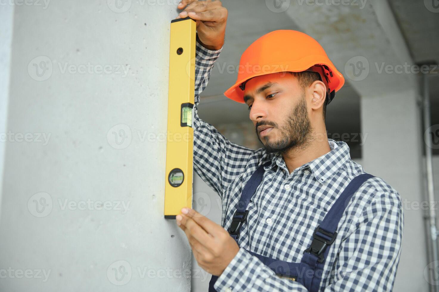 Indian male construction worker standing in uniform and hard hat at construction site. photo
