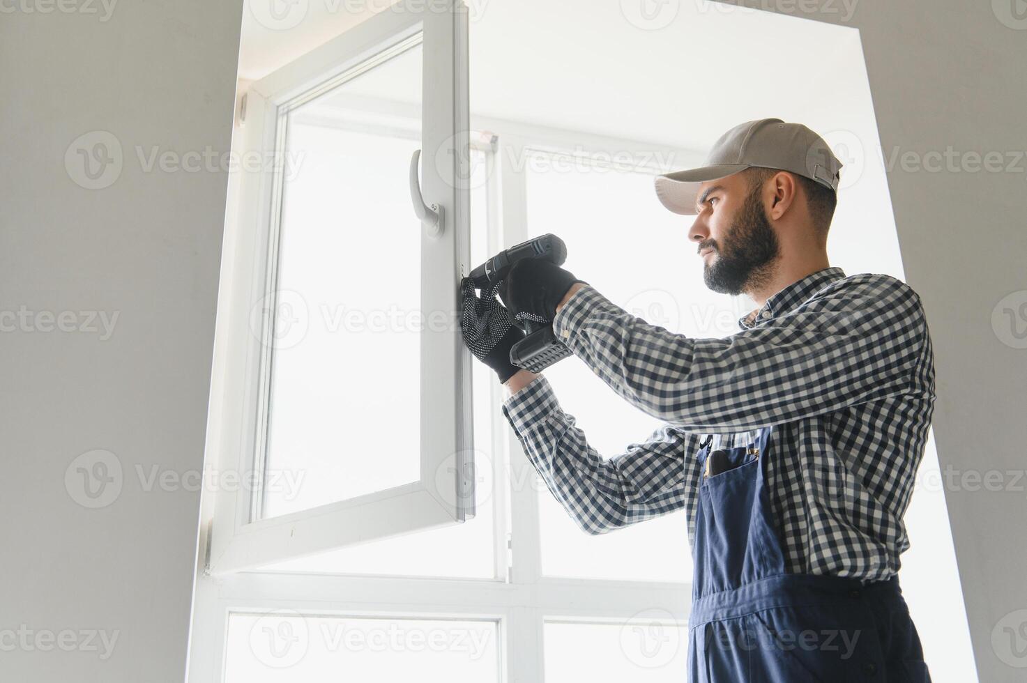 Workman in overalls installing or adjusting plastic windows in the living room at home photo
