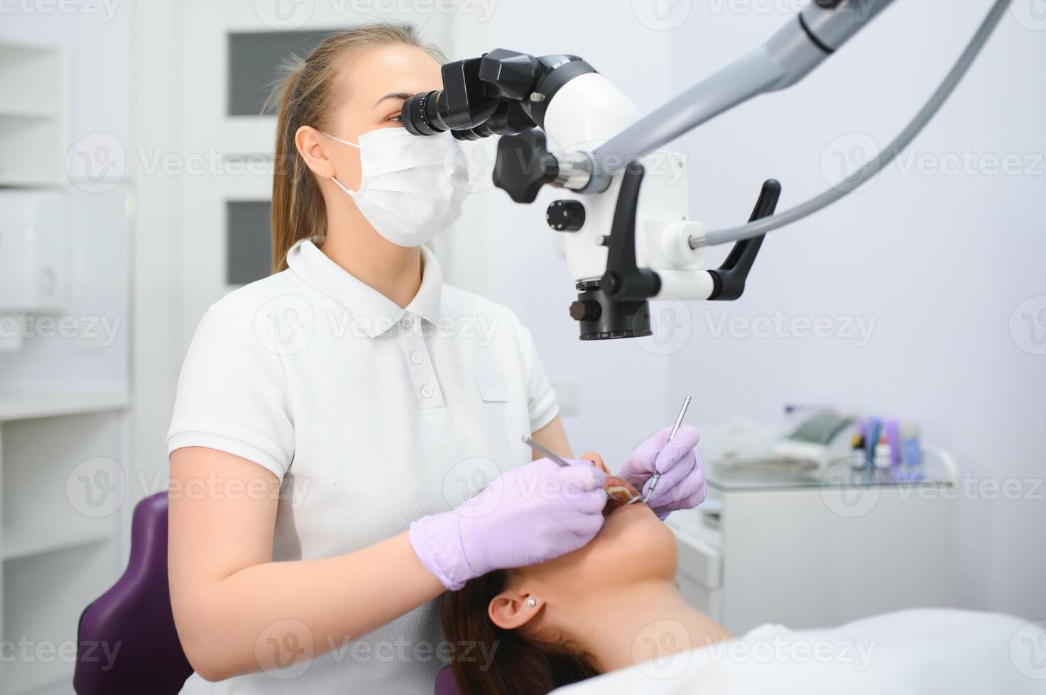 Female dentist using dental microscope treating patient teeth at dental clinic office photo