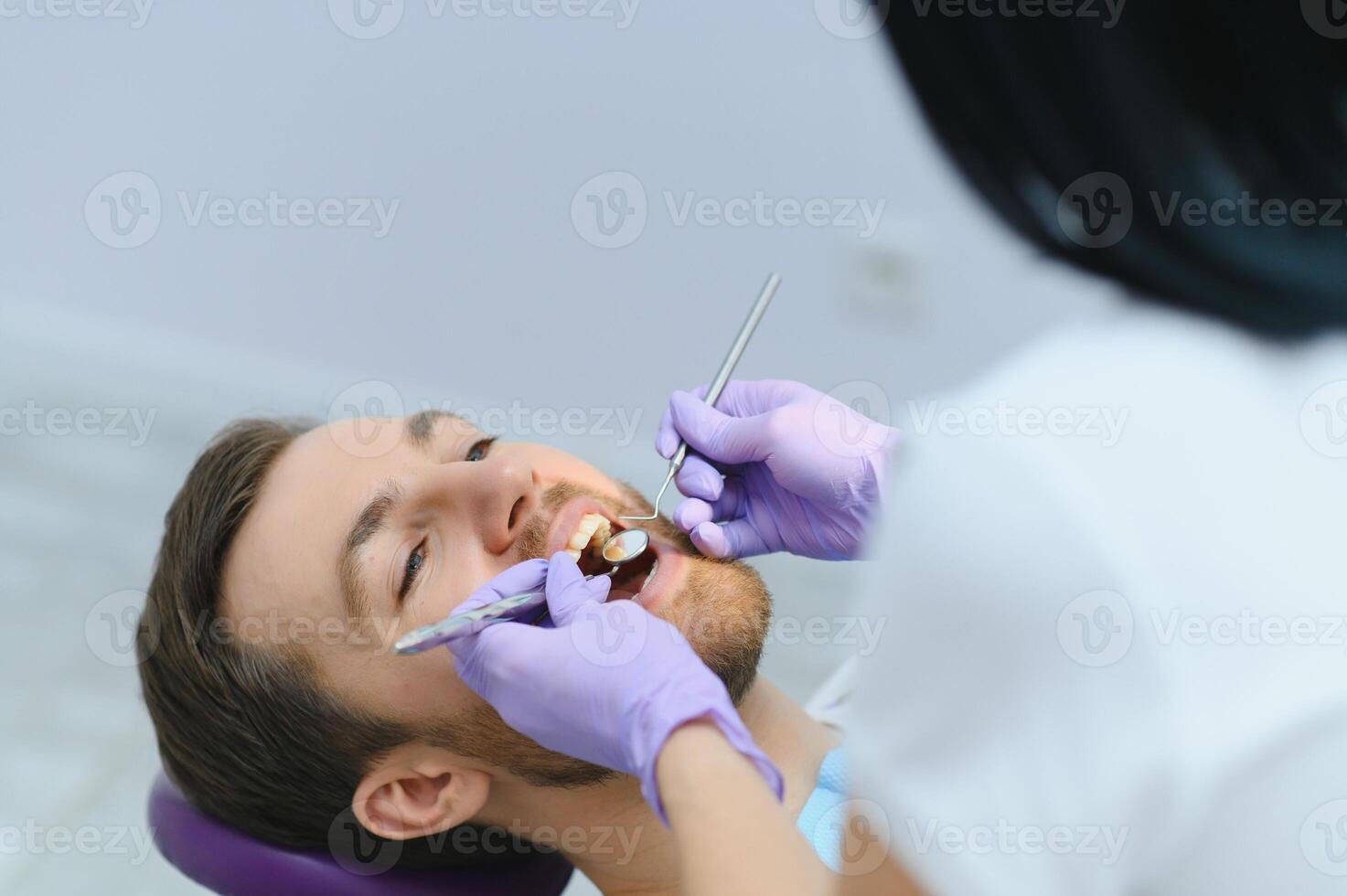 Periodontal Services. Closeup Shot Of Smiling Man Getting Treatment In Stomatologic Clinic, Dentist Doctor In Gloves Using Sterile Dental Tools For Examining Teeth Of Male Patient photo