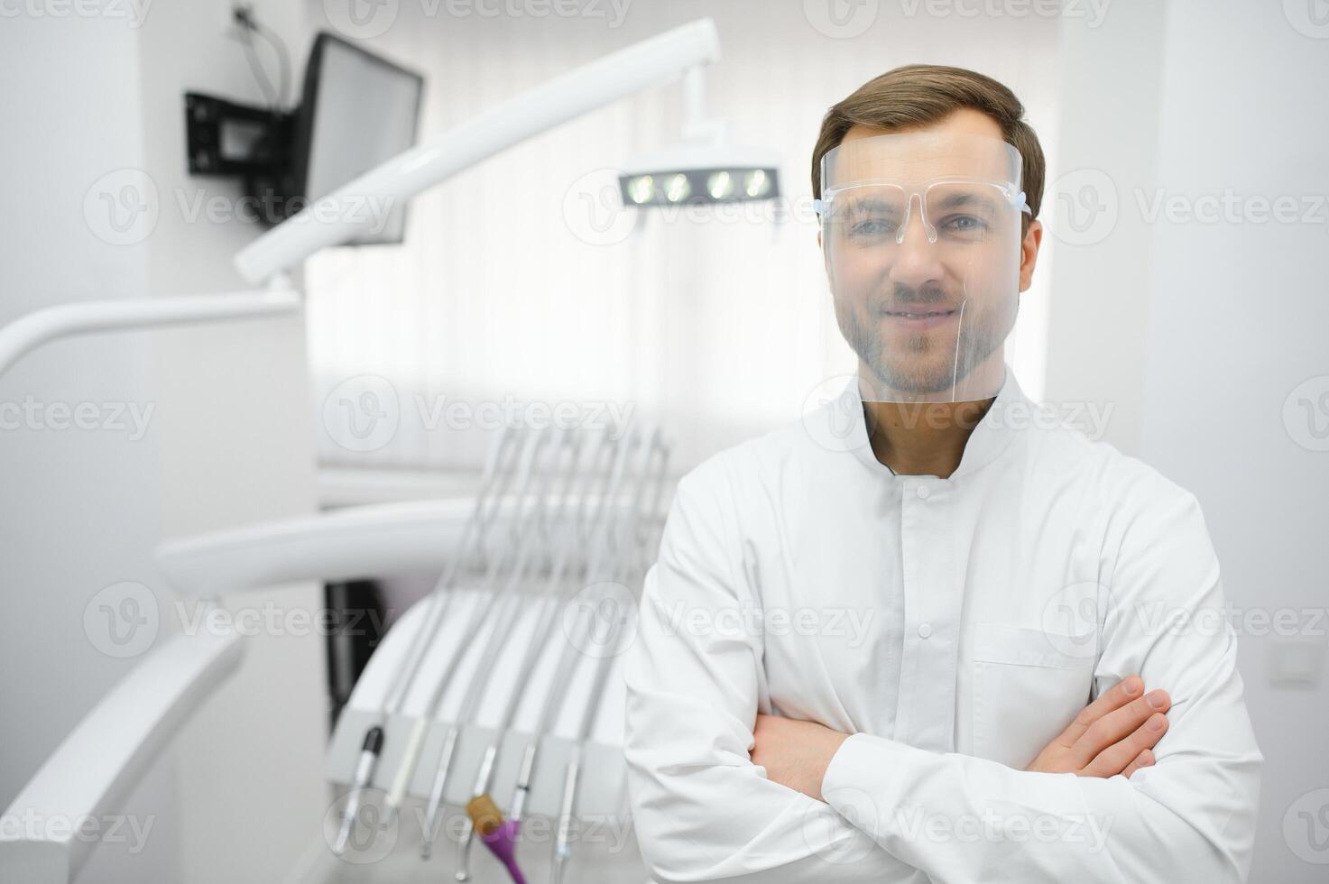 Attractive male dentist in doctors white lab coat posing in modern dental office photo