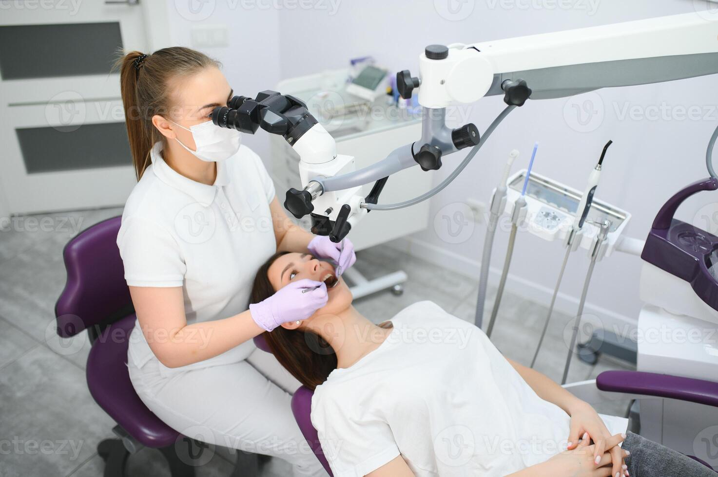 Female dentist using dental microscope treating patient teeth at dental clinic office photo