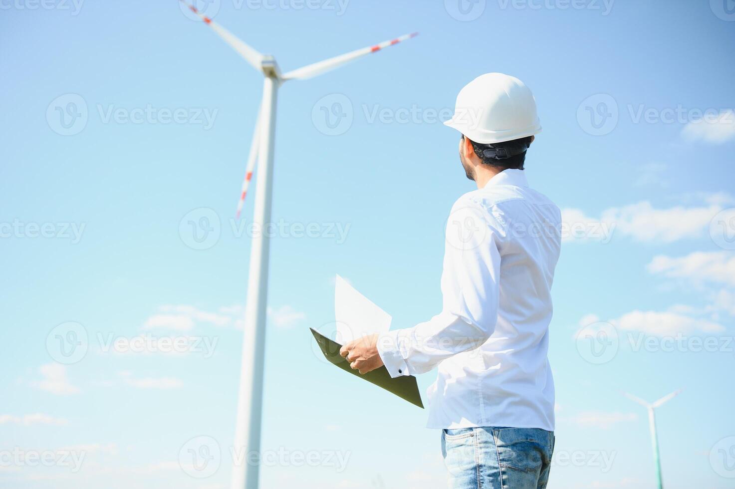 Engineer India man working at windmill farm Generating electricity clean energy. Wind turbine farm generator by alternative green energy. Asian engineer checking control electric power photo