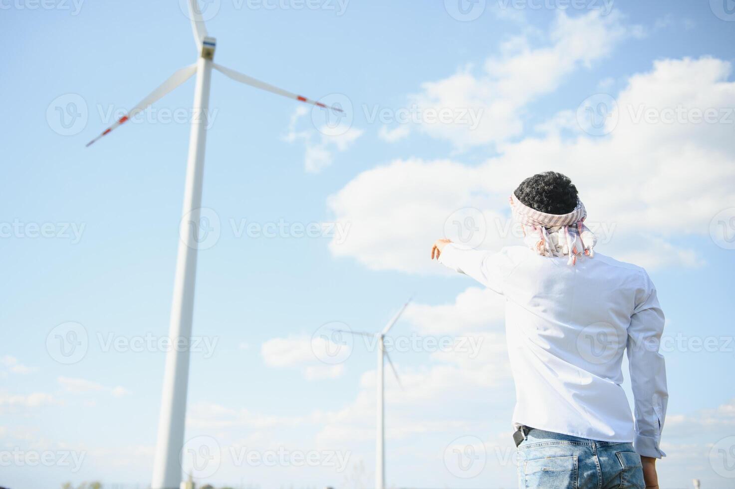 Engineer India man working at windmill farm Generating electricity clean energy. Wind turbine farm generator by alternative green energy. Asian engineer checking control electric power photo