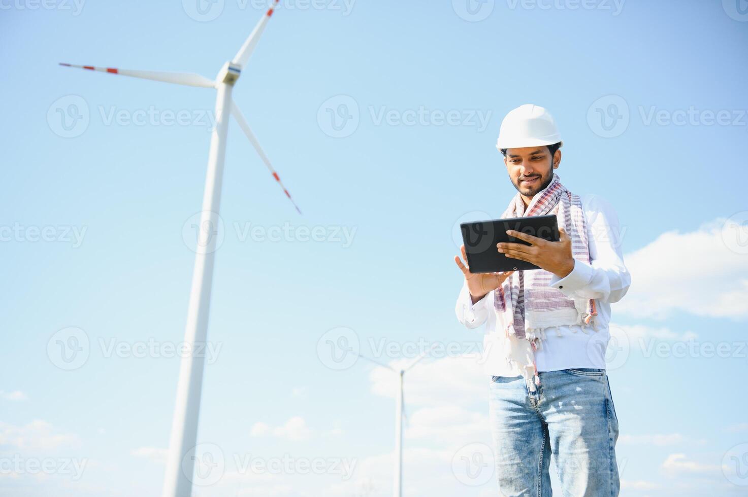 Engineer India man working at windmill farm Generating electricity clean energy. Wind turbine farm generator by alternative green energy. Asian engineer checking control electric power photo