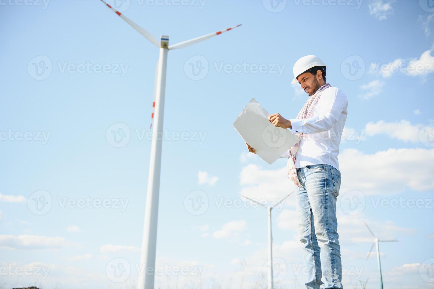 Engineer India man working at windmill farm Generating electricity clean energy. Wind turbine farm generator by alternative green energy. Asian engineer checking control electric power photo