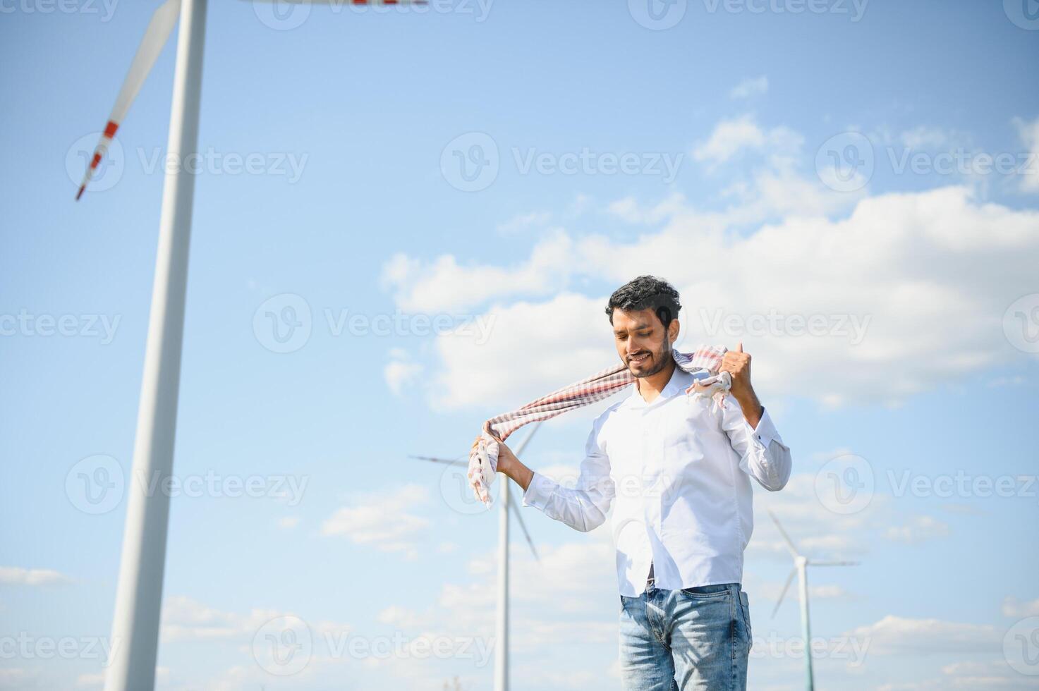 Engineer India man working at windmill farm Generating electricity clean energy. Wind turbine farm generator by alternative green energy. Asian engineer checking control electric power photo