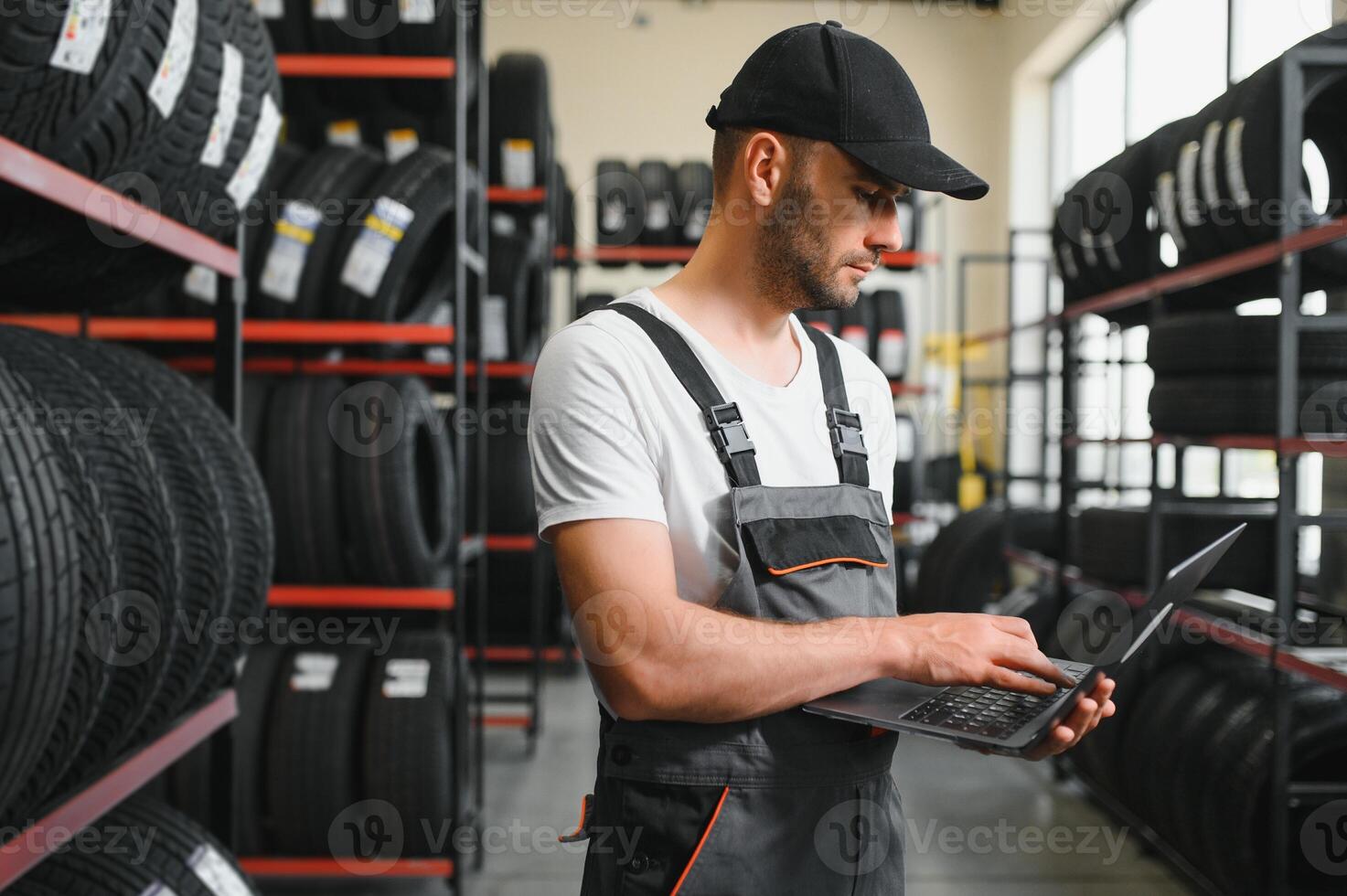confident mechanic man checking characteristics of tyre in auto service shop photo