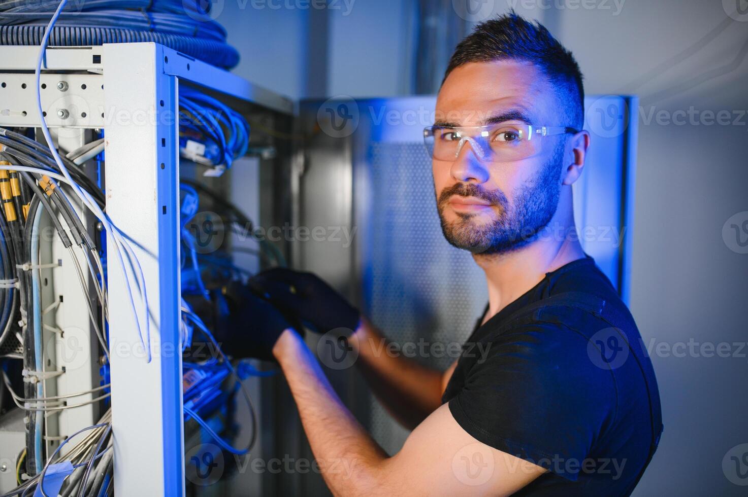 A technician works with server equipment in a data center. A man commutes wires in a server room photo