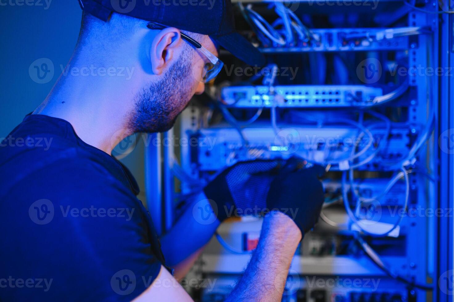 Young man is working with internet equipment and wires in server room photo