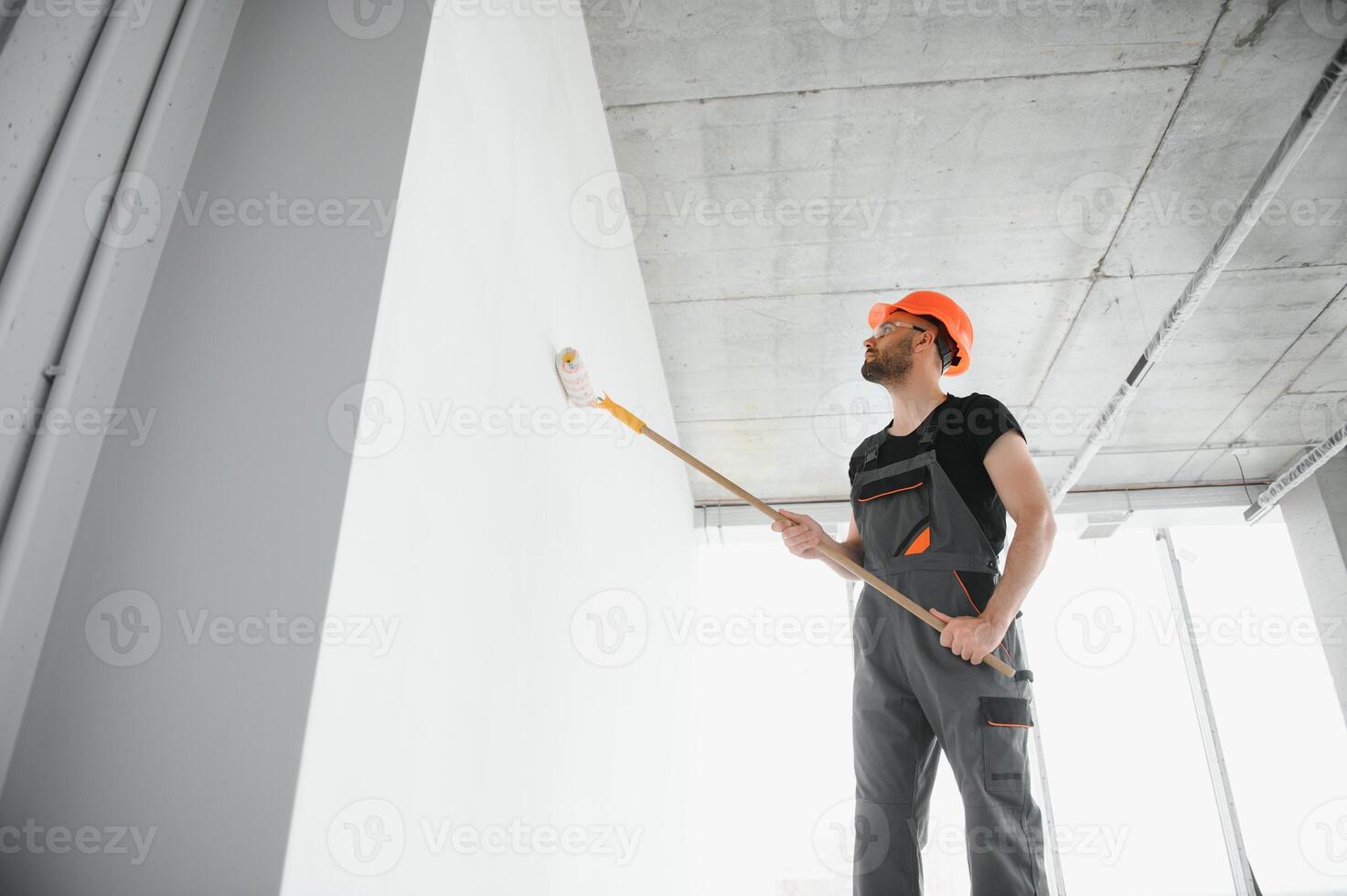 Portrait of man holding paint roller while painting white wall and making renovation photo