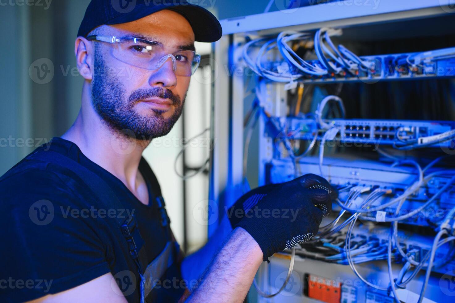 Young man is working with internet equipment and wires in server room photo