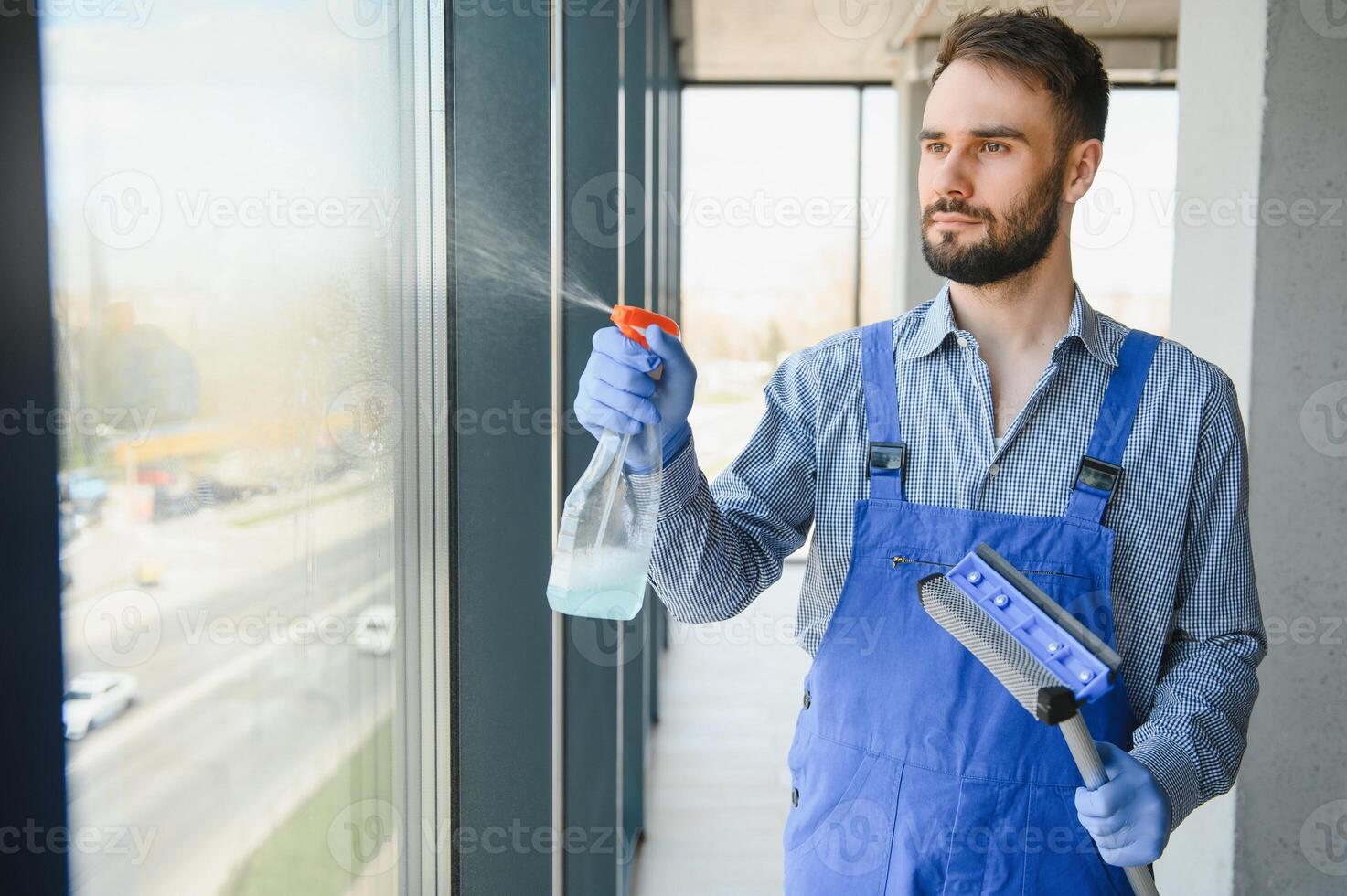 Male professional cleaning service worker in overalls cleans the windows and shop windows of a store with special equipment photo