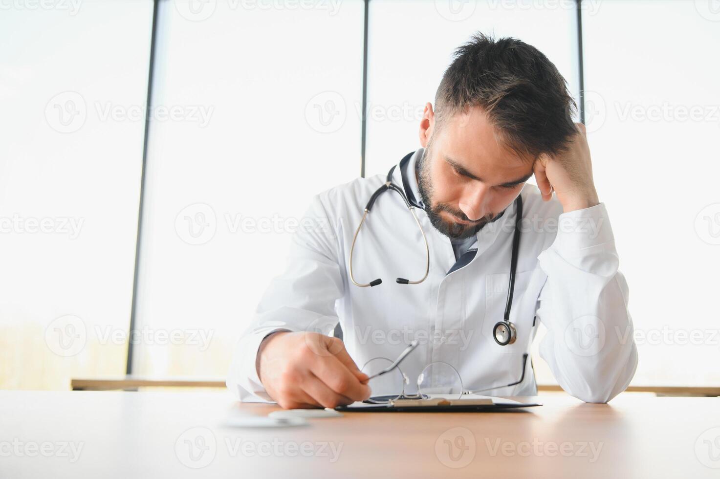 Doctor man sitting at the desk at his working place. Perfect medical service in clinic. Portrait of a handsome young doctor. photo