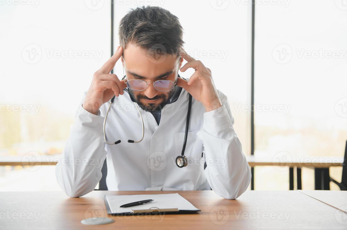 Close-up of upset tired medical worker closing head with hands. Depressed male doctor sitting in office. stethoscope on persons neck. Modern medicine and healthcare concept. photo
