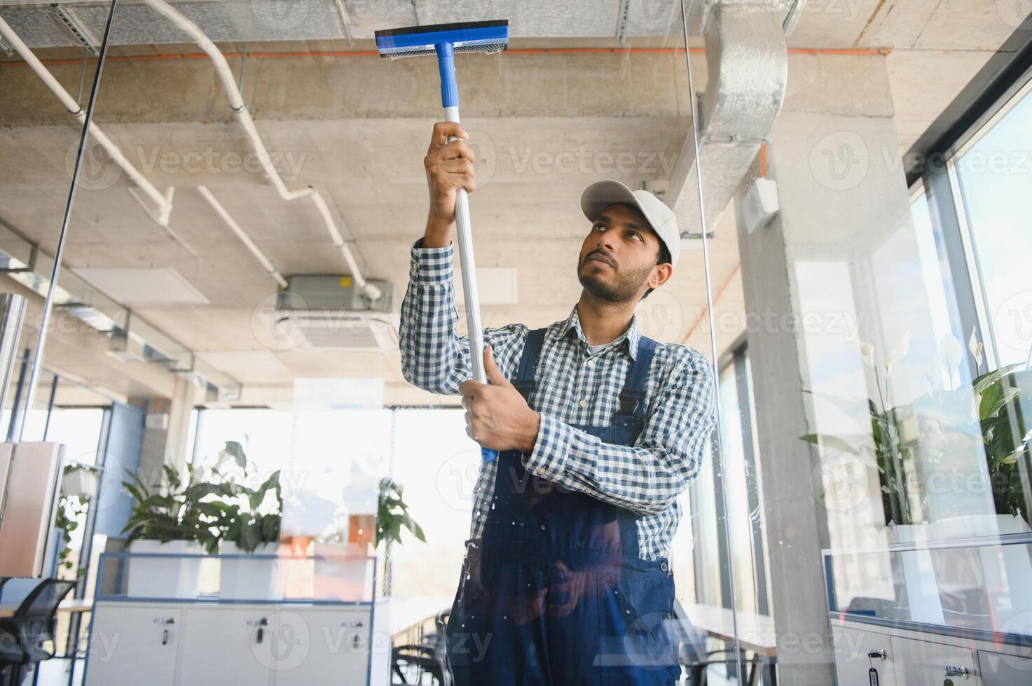 Young indian man washing window in office photo