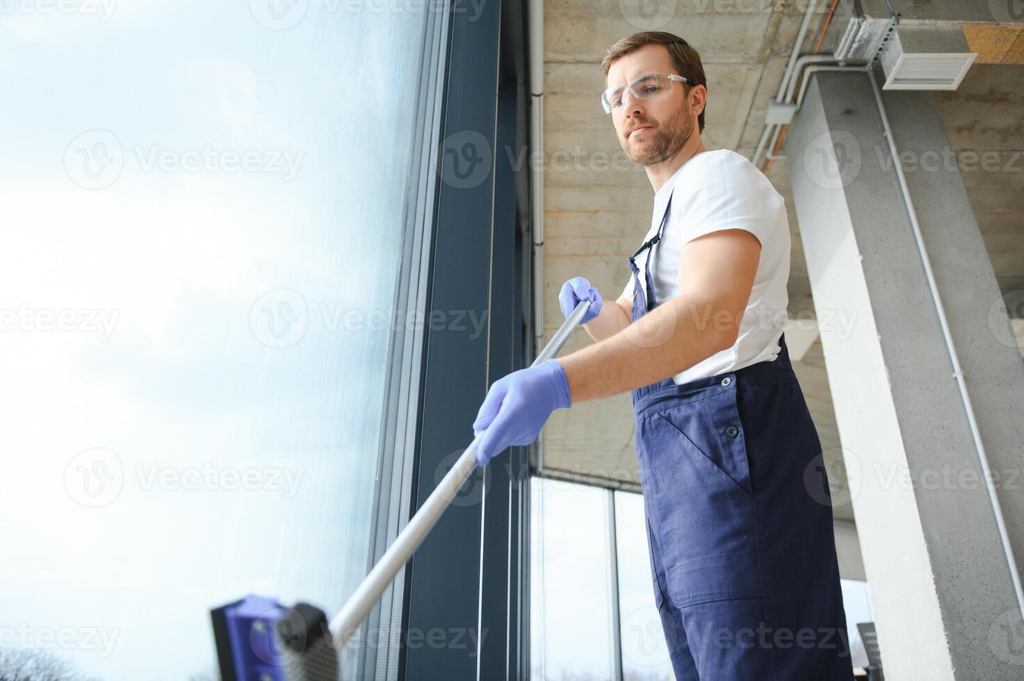 Male professional cleaning service worker in overalls cleans the windows and shop windows of a store with special equipment. photo