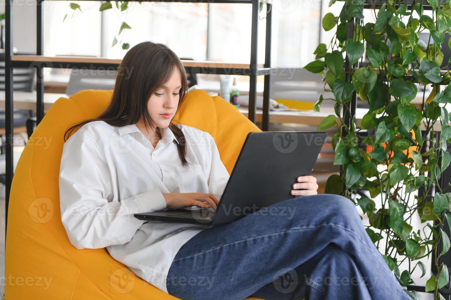 A beautiful caucasian female student is studying in college remotely. She is sitting with a laptop and a notepad and concentrated is watching a conference lesson photo