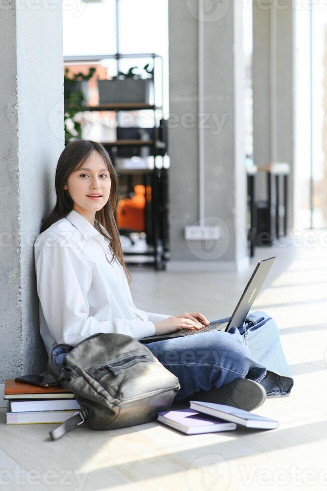 A beautiful caucasian female student is studying in college remotely. She is sitting with a laptop and a notepad and concentrated is watching a conference lesson photo