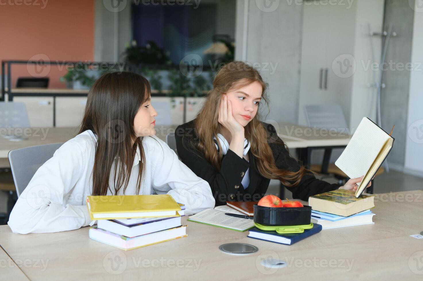 Two fifteen-year-old schoolgirls reading books and taking abstract in copybooks are doing homework in the school library photo