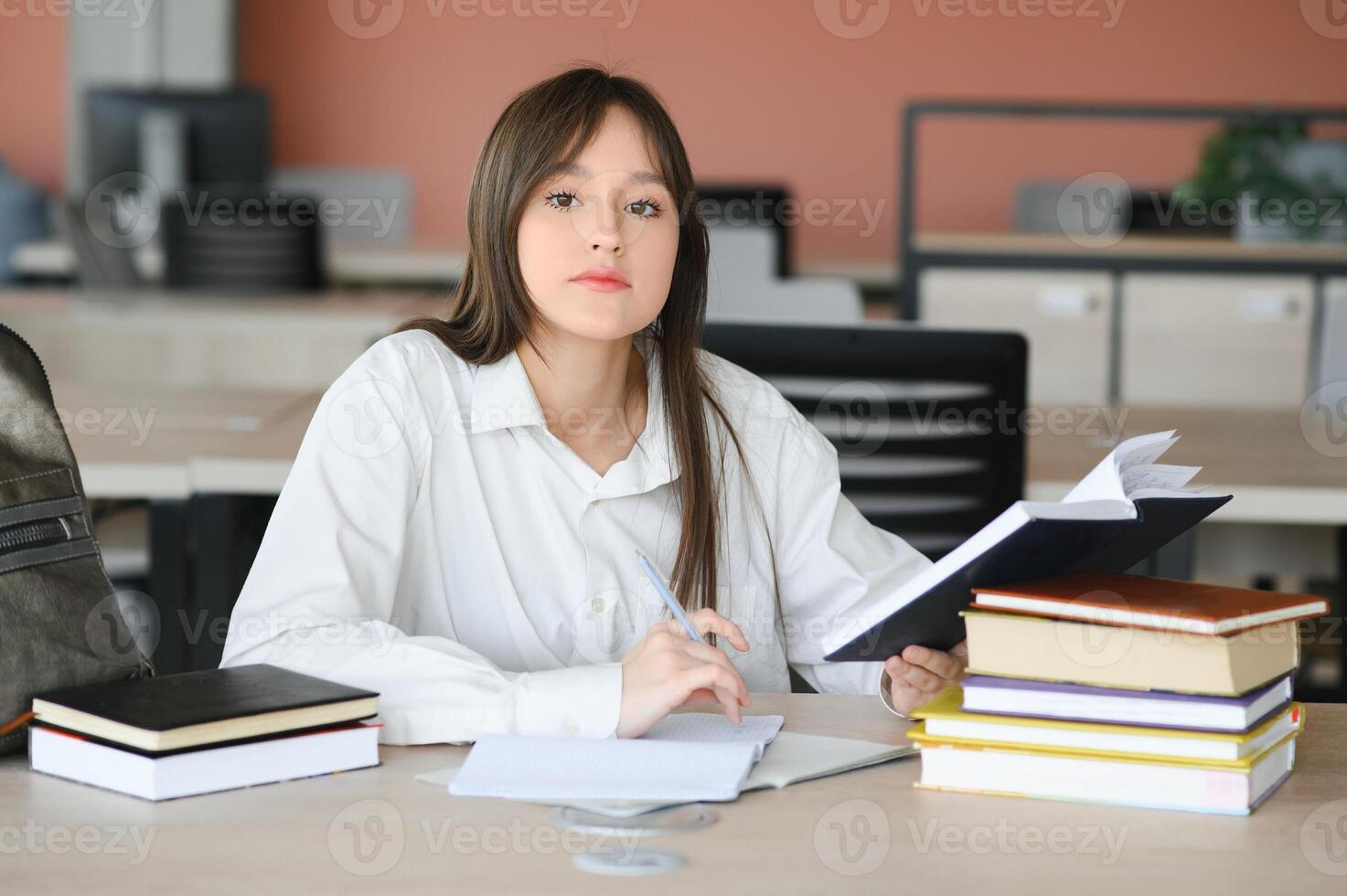 Teen girl studying with textbook writing essay learning in classroom. photo
