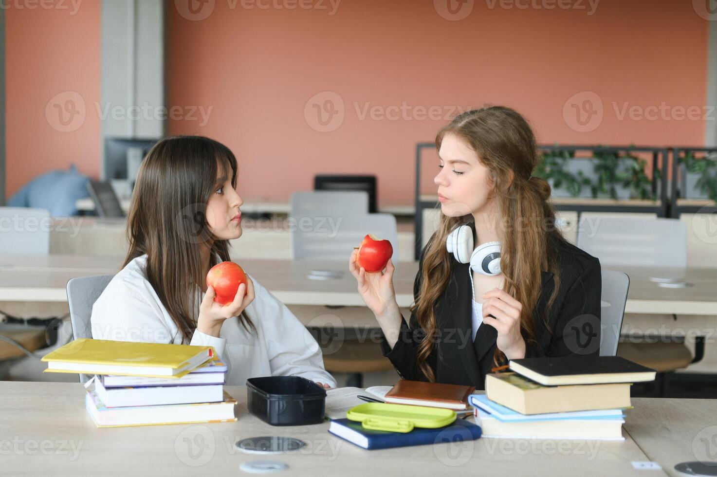 Two happy smiling female students are sitting and eating apples, studying and preparing for exams. photo