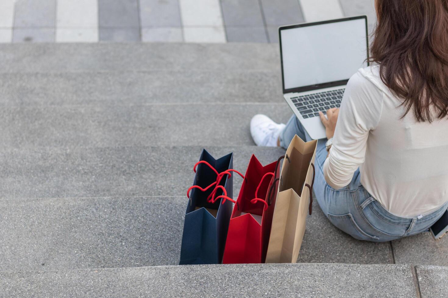 Blur image,young woman checks work from laptop on front steps of department store after she goes shopping. Shopping ideas during New Year's Eve sale to get great products at affordable prices photo