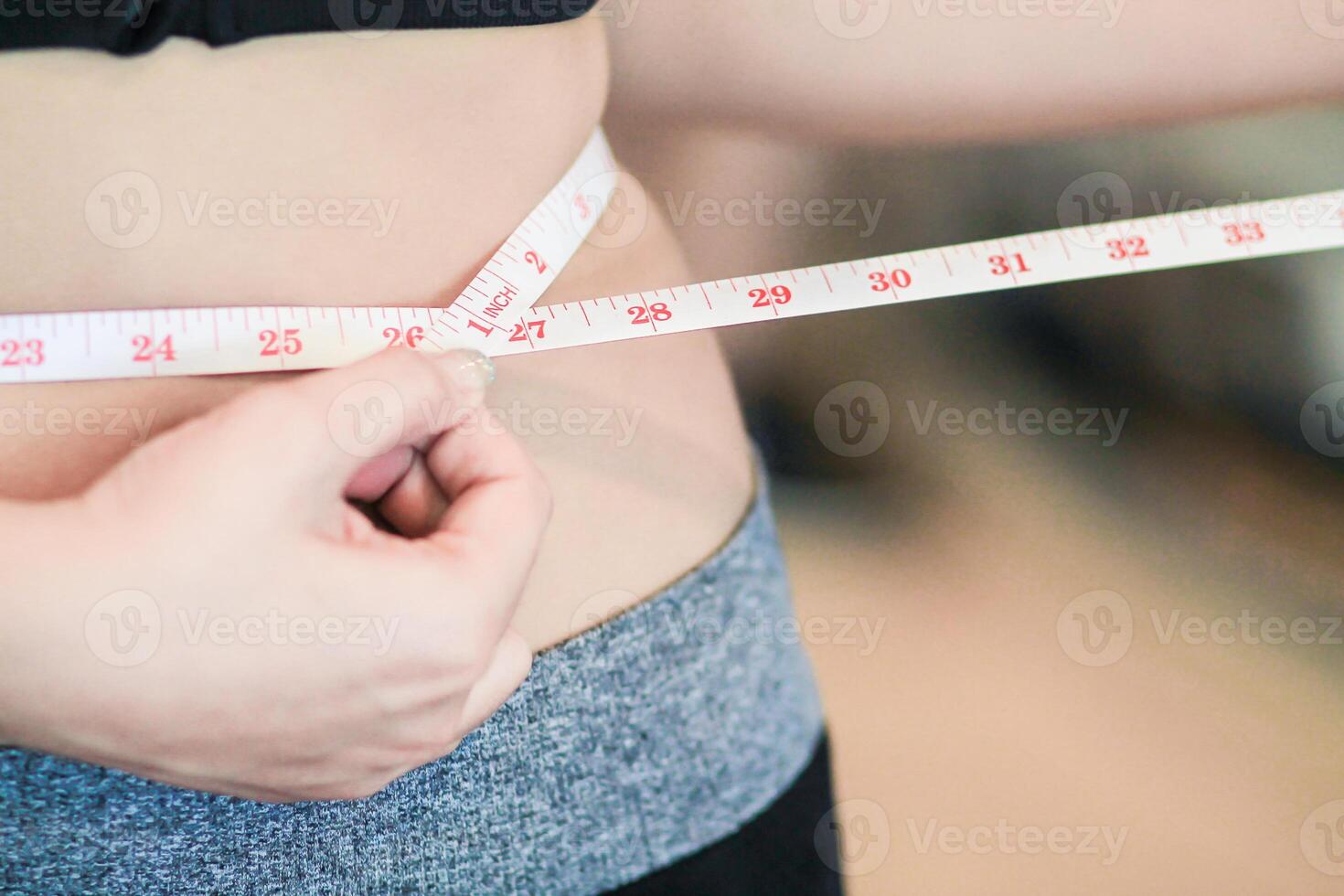 A young woman holds a tape measure to measure her waist circumference after exercising to reduce belly fat and measures her waist circumference to check the results of the weight loss course. photo