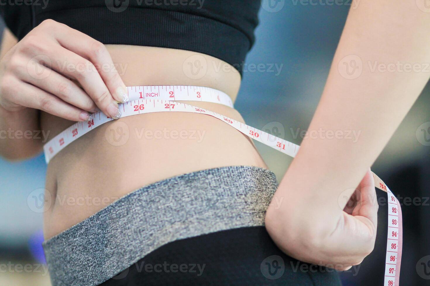 A young woman holds a tape measure to measure her waist circumference after exercising to reduce belly fat and measures her waist circumference to check the results of the weight loss course. photo
