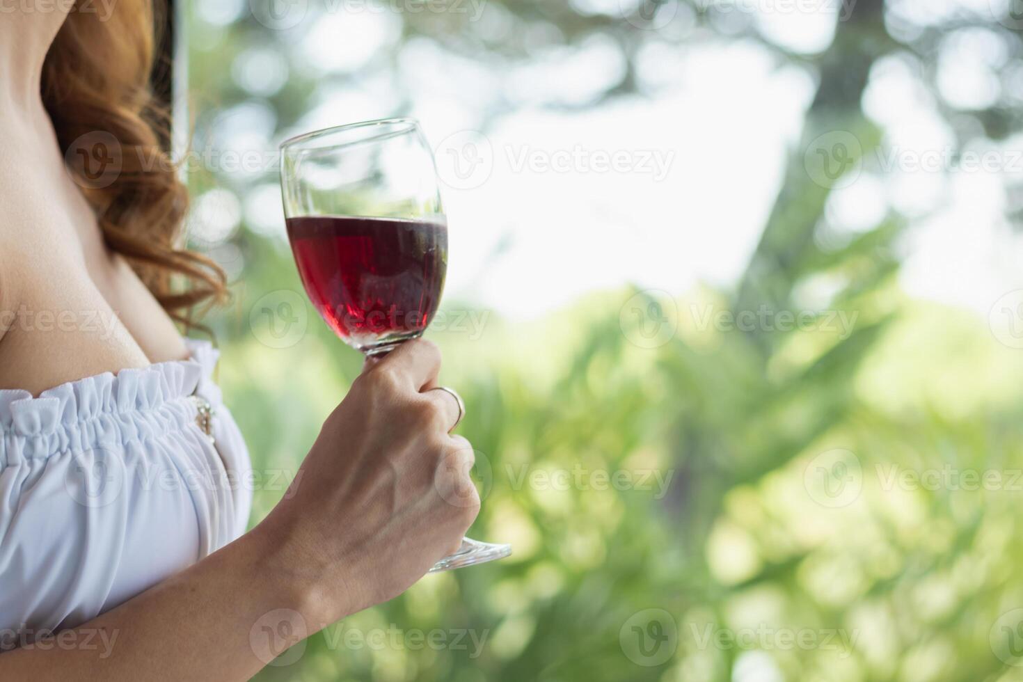 young woman raises glass of red wine by pool at resort where she enjoyed stay to celebrate her successful business. young woman is drinking wine to celebrate her successful business venture by pool. photo