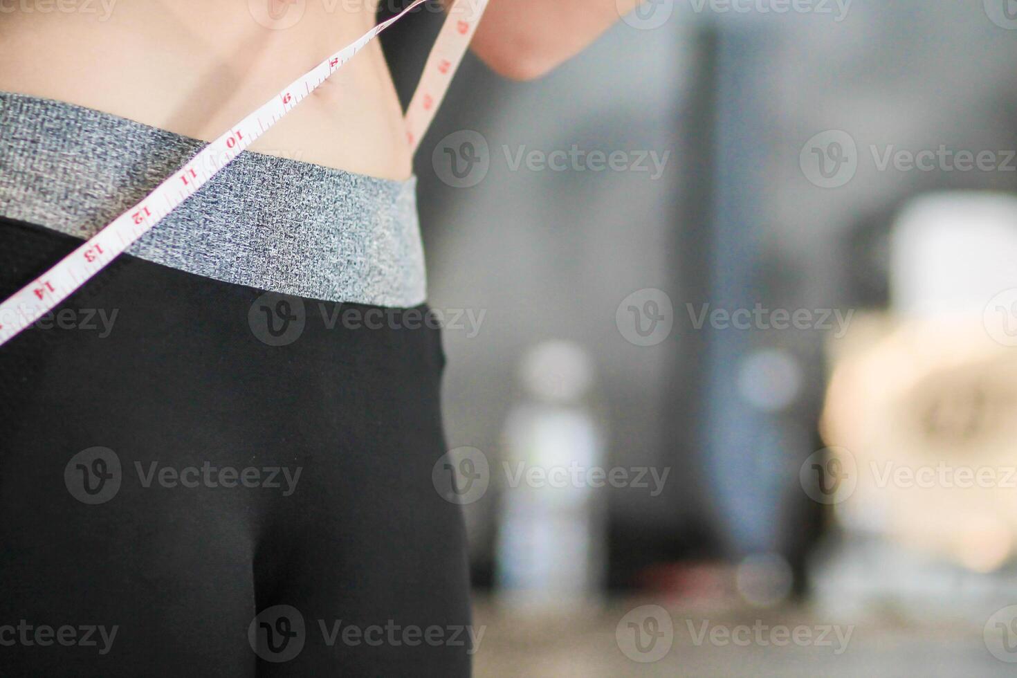 A young woman holds a tape measure to measure her waist circumference after exercising to reduce belly fat and measures her waist circumference to check the results of the weight loss course. photo