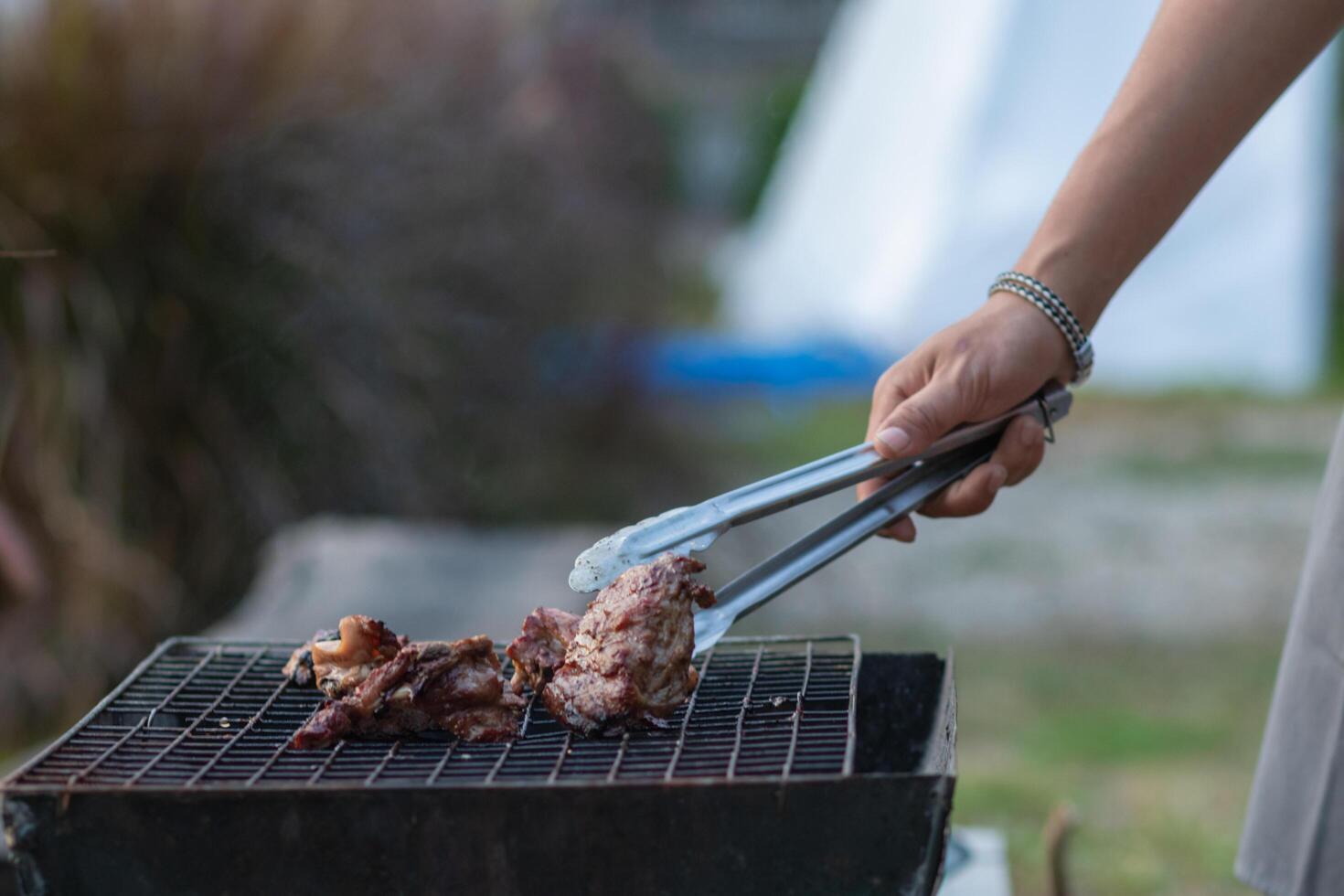 The meat is grilled on a metal grill over charcoal grill to be cooked. It's a fun BBQ during the holidays and out camping with the family. Barbecuing is a popular dish during celebrations and camping. photo
