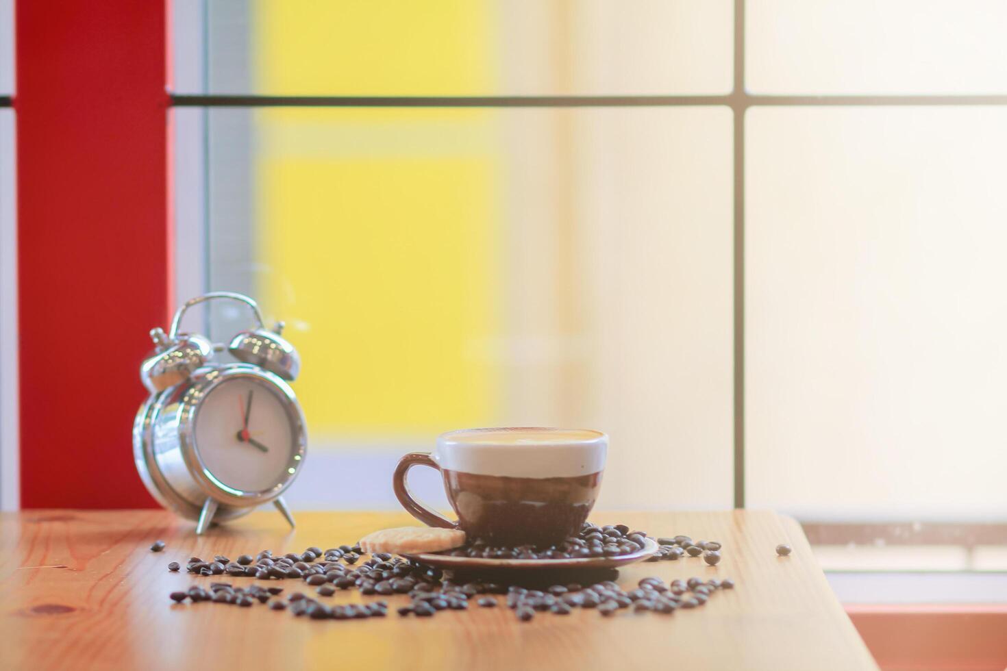 The alarm clock set by the window in the morning beside the coffee cup is used to set the time to remind appointments, is an analog alarm clock that sends alarms by tapping the side bell. photo