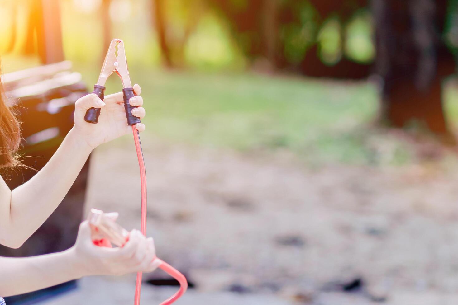 A woman holding a black and red Jumper cable that shows the positive and negative terminals to be used as a connector to stimulate the car battery to be started.Concept of car battery stimulation photo