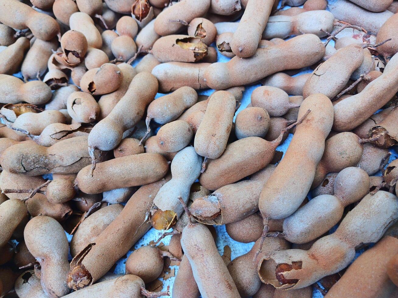 Ripe tamarind fruit and some tamarind seeds on a wooden woven board. photo