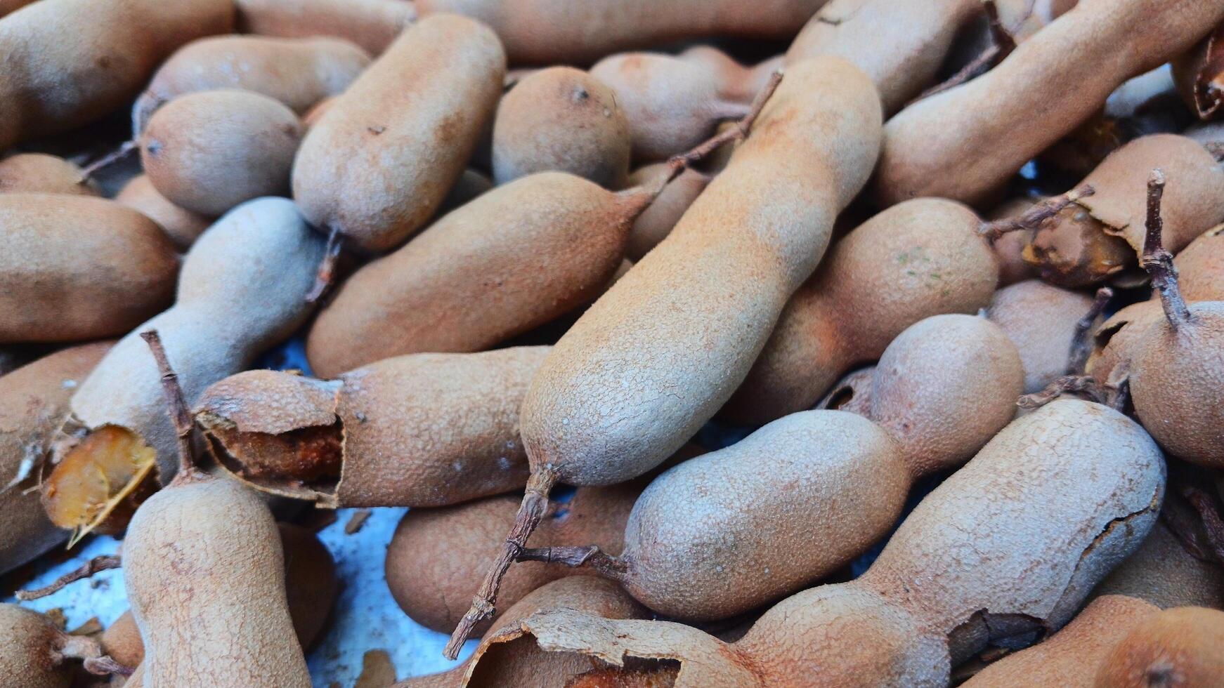 Ripe tamarind fruit and some tamarind seeds on a wooden woven board. photo