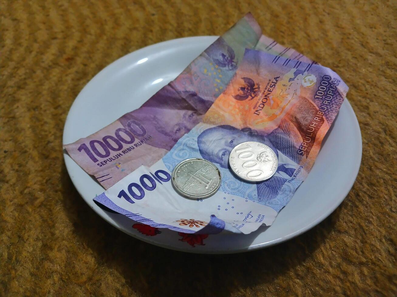 Ceramic cup with red rose motif and Indonesian rupiah banknotes on yellow carpet background photo