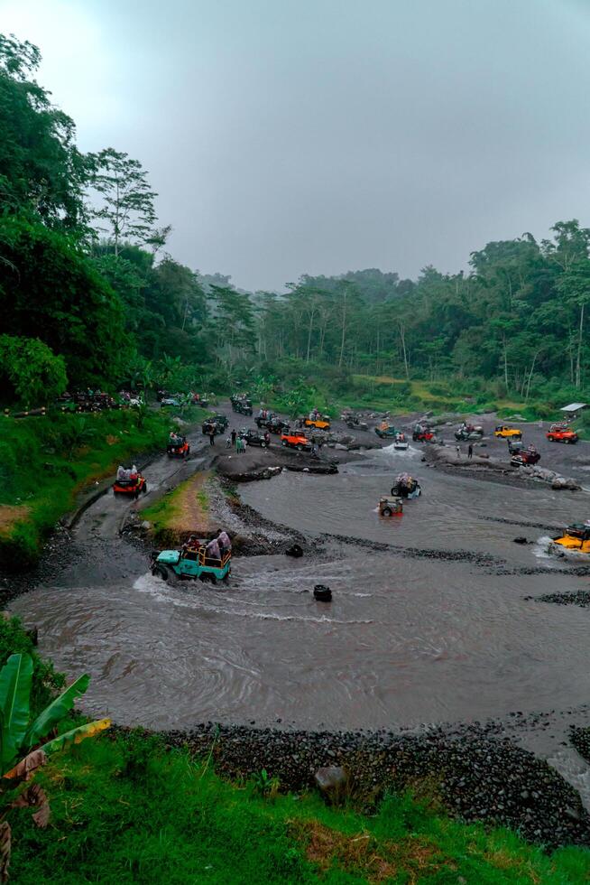 Yogyakarta, Indonesia, 2024 - Crossing the river in a high-speed jeep until the water splashes in all directions and wets the passengers. Offroad driving tourist jeep during holiday season photo