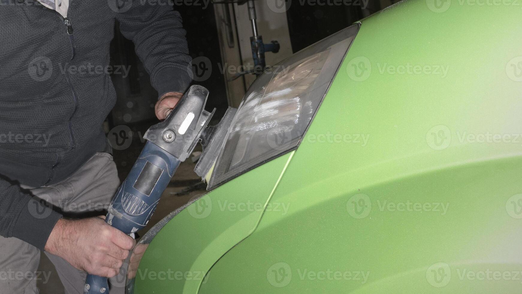 Car headlight polishing. A worker with an electric polisher polishes darkened headlights photo