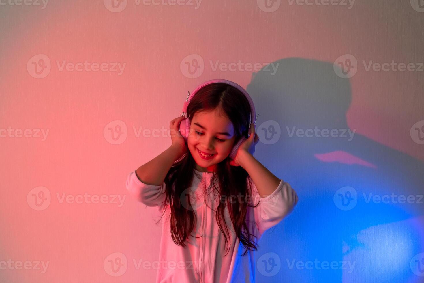 A happy little girl in headphones listening to music in neon light photo