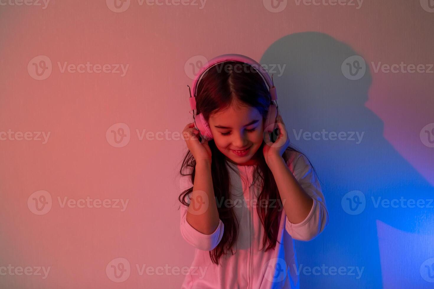 Beautiful happy little girl in headphones listening to music in neon light photo