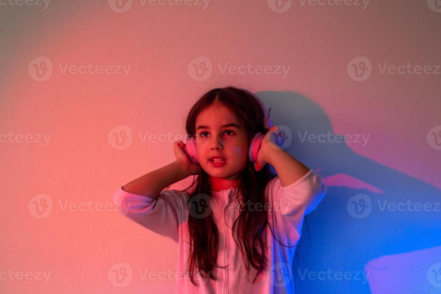 Beautiful little girl in headphones listening to music in neon light photo