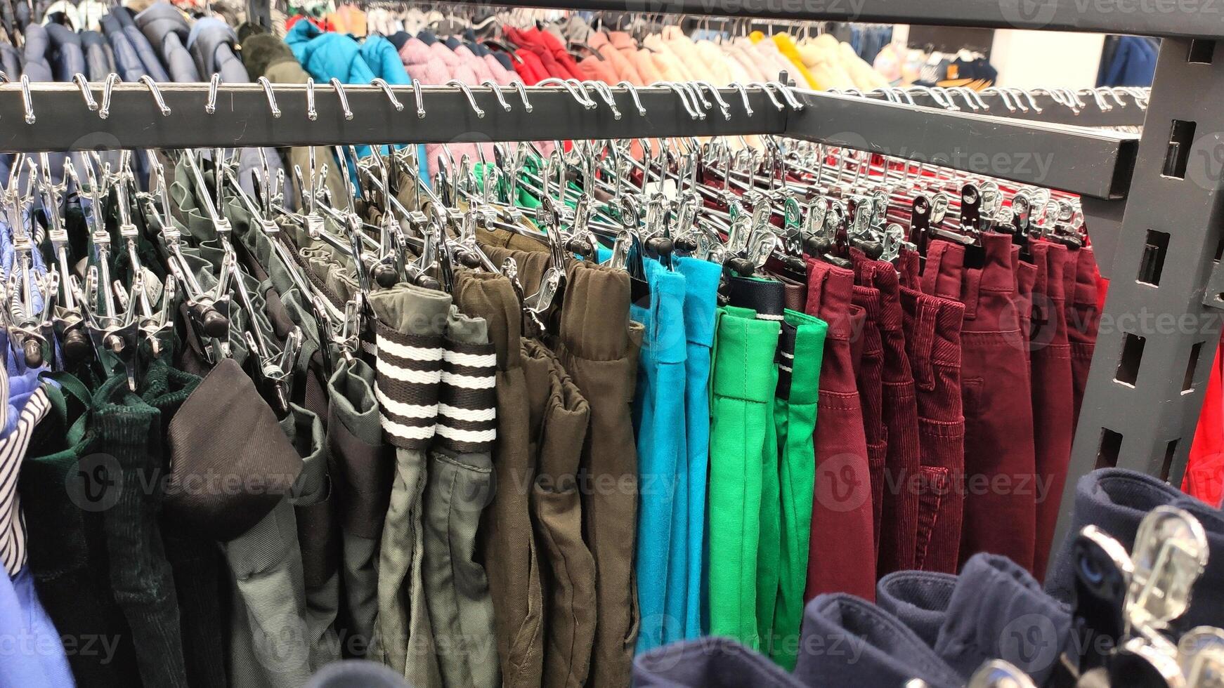 Row of different colorful pants trousers on hanger in shop, photo