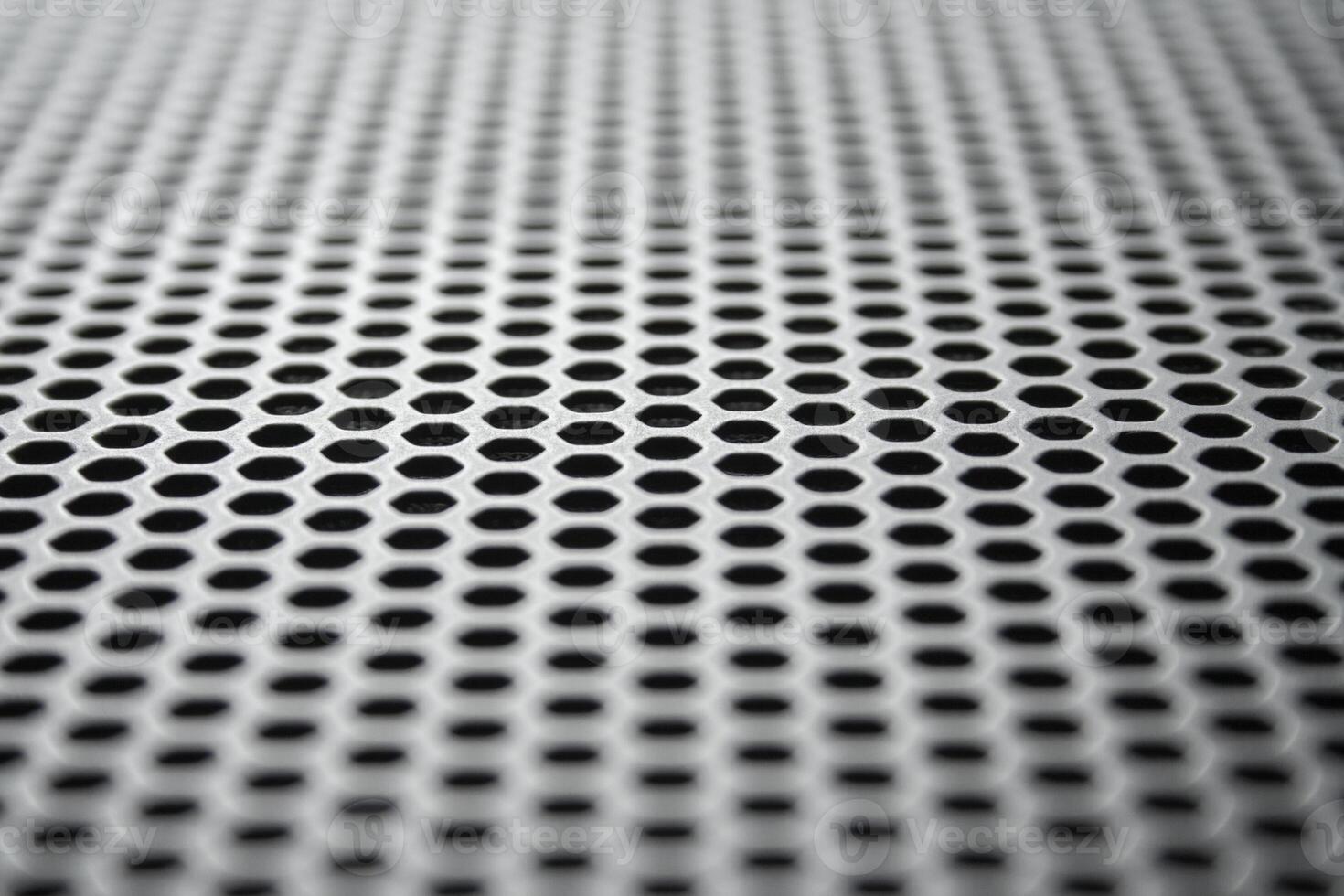 Perspective view on a the metal surface with regular round holes. Industrial background photo