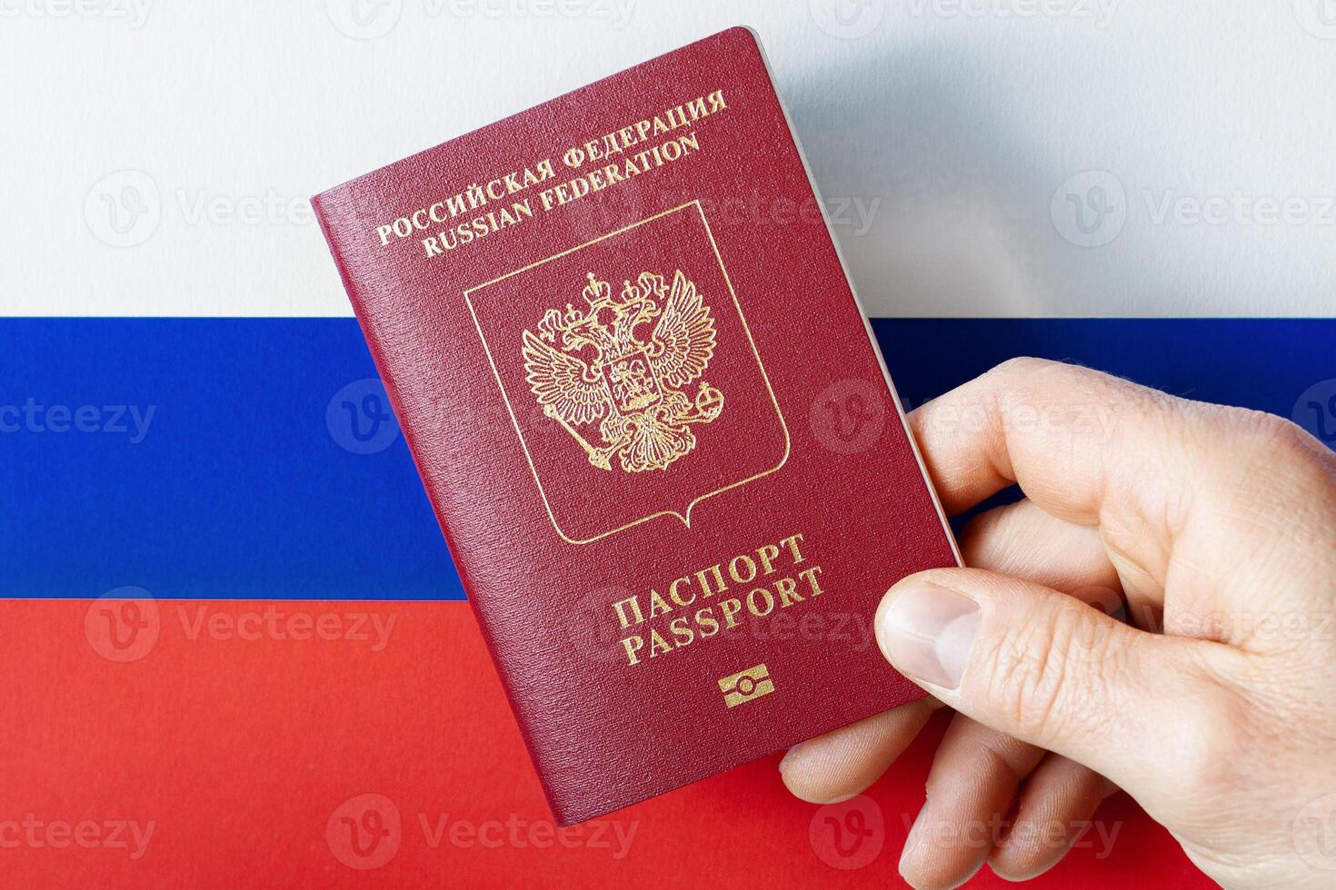 A man's hand holds a International passport of the Russian Federation on a background of national flag photo