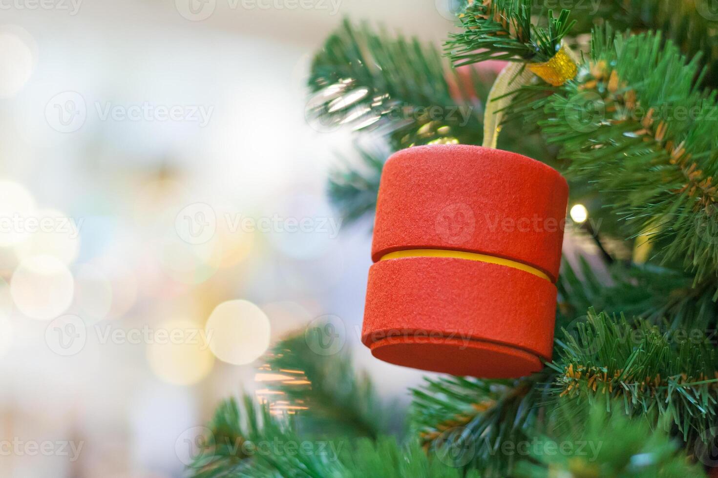 Close-up view of a Christmas tree decoration, in the shape of a red cylinder with blurred lights in bokeh on a background photo